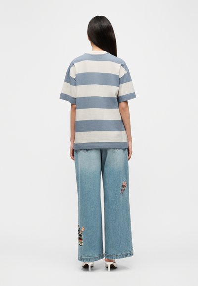 T-shirt à manches courtes rayé en bleu clair et beige, associé à un jean denim à jambes larges avec des détails brodés et un ourlet effiloché.