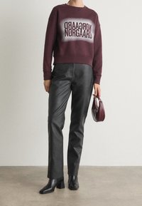 Sweatshirt bordeaux avec imprimé graphique blanc, associée à un pantalon en cuir noir et des bottes à talons noires. Accessoires comprenant un petit sac bordeaux.