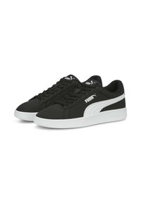 Baskets de sport noires avec des accents blancs, en matériau synthétique lisse, bout rond, système de laçage et semelle blanche rembourrée.