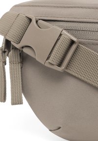 Beige szövet tasak, textúrált felülettel, műanyag csattal és szőtt pánttal, biztonságos záródásra és hordozhatóságra tervezve.