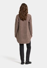 Bruine fleece lange mouwen jas met een gestructureerde afwerking, met een afgeronde zoom en verlaagde schouders, gedragen over zwarte broek en zwarte laarzen.