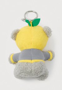 Μαλακό μπρελόκ με γκρίζο αρκουδάκι που φοράει ένα κίτρινο καπέλο σε σχήμα λεμονιού με πράσινα φύλλα φελτ, με θέα από πίσω.