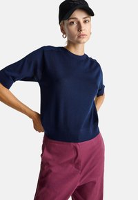 Granatowy, dzianinowy top z krótkim rękawem, z ribbowanym okrągłym dekoltem i dopasowaną talią; zestawiony z bordowymi spodniami, minimalistyczny design, teksturowana tkanina.