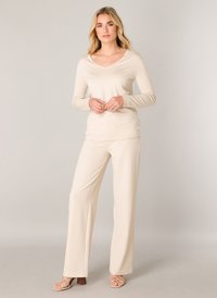 Beige Langarmoberteil mit V-Ausschnitt, kombiniert mit beigen weiten Hosen, beide aus weichem Stoff gefertigt. Getragen mit beigen Riemchensandalen.