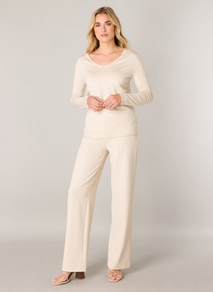 Beige lange mouw top met een V-hals, gecombineerd met ruime beige broek, beide gemaakt van zachte stof. Draag het met beige hakken met bandjes.