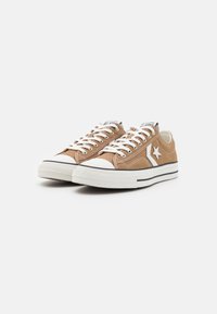 Sneakers in tela marrone con accentuazioni bianche, dotati di tacco di gomma, lacci bianchi piatti e suola a strisce bianco e nere.