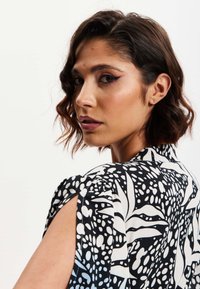 Black and white patterned blouse featuring large leaf designs and polka dots, with short sleeves and a relaxed fit.