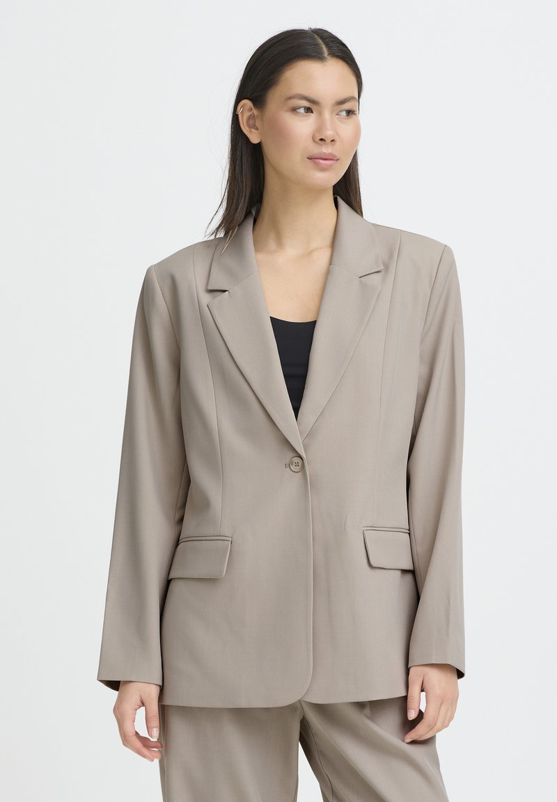 Blazer beige avec une fermeture à bouton unique, des revers à encoche, deux poches avant et une coupe ajustée. Fabriqué dans un tissu lisse avec une texture subtile.