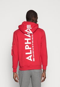 Felpa con cappuccio rossa e grande logo bianco "ALPHA INDUSTRIES" sulla schiena, maniche lunghe, polsini a coste e tasca a marsupio.