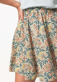 Jupe florale avec une taille élastique, présentant un fond crème et un motif floral multicolore dans des teintes de rose, jaune et vert.