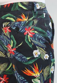 Pantaloni corti floreali con uno sfondo nero caratterizzati da vivaci fiori tropicali e foglie. Realizzati in tessuto con una texture liscia, includono una tasca posteriore.