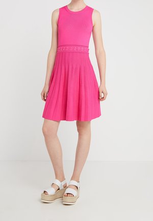 Ärmelloses, knallpinke Kleid mit plissiertem Rock und Lochgürtel-Detail, kombiniert mit weißen Plateau-Sandalen mit Knöchelriemen.