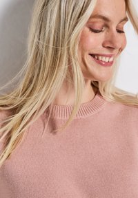 Jasnoróżowy dziany sweter z okrągłym prążkowanym dekoltem i delikatną fakturą, z miękkimi włóknami i subtelnymi detalami ściegów.