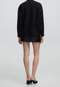 Zwarte sweatshirt met ribbels aan de manchetten, ronde hals en een relaxed fit, gecombineerd met een zwarte mini rok. Glad textuur; slanke, moderne silhouette.