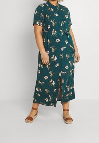 Groene jurk met bloemenprint, korte mouwen, knoopsluiting aan de voorkant, cinched taille en zijsplitten. Draag met bruin sandaaltjes met bandjes.