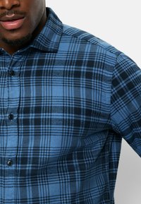 Karierte Hemd in Blau mit Knöpfen, das kontrastierende dunkelblaue und hellblaue Kästchen zeigt, mit einem Standardkragen und glatter Textur.