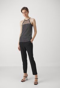 Melna acs halter tops ar krāsainu punktu rakstu, kombinēta ar melniem piegriezuma biksēm un melnām siksnu papēžkurpēm. Gluda tekstūra un pieguļoša forma.