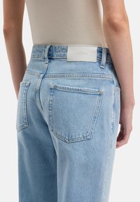 Jeans in denim azzurro chiaro con vita alta, cinque tasche, cuciture sottili e un'etichetta con marchio sulla fascia della vita posteriore.