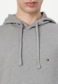 Pilkas gobtuvu pasidarytas iš minkštos medžiagos su kengūros kišene. Yra raištelių gobtuvas ir mažas siuvinėtasis logotipas ant krūtinės.