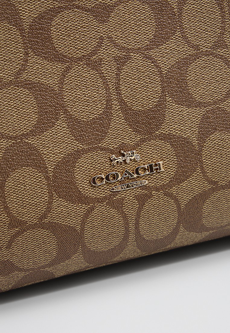 Borsa di tessuto marrone con un motivo testurizzato di cerchi intrecciati. Presenta un logo dorato "COACH NEW YORK".