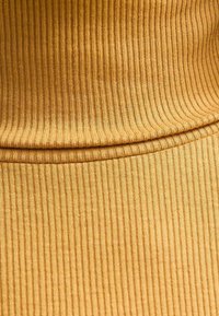 Tessuto a coste di tonalità giallo dorato, caratterizzato da una texture liscia e linee ritmiche. Il design è aderente, con una sensazione morbida ed elastica.