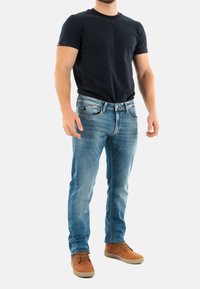 Jeans de mezclilla azul con un corte recto, combinados con una camiseta negra de manga corta y zapatos marrones. Diseño sencillo y estilo casual típico.