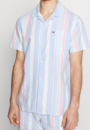Homme portant une chemise à manches courtes avec des rayures verticales pastel en bleu, rose, jaune et violet, dotée d'une poche poitrine et d'un col.