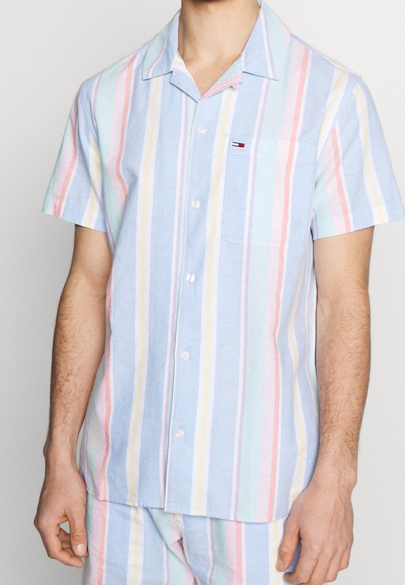 Homme portant une chemise à manches courtes avec des rayures verticales pastel en bleu, rose, jaune et violet, dotée d'une poche poitrine et d'un col.