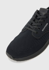 Baskets en mesh noir avec une surface texturée, bout rond et design à lacets. Présentent le logo "Tommy Hilfiger" sur le côté et la languette.