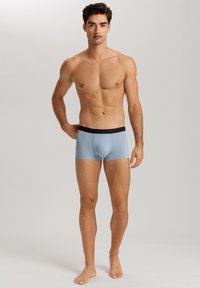 Ljusblå boxershorts med svart midja, med en åtsittande design och slät textur. Exponerad sömdetalj framtill.
