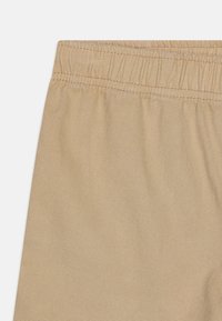 Tissu beige avec une surface texturée, doté d'une ceinture élastique en haut. Le matériau semble léger et flexible.