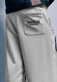 Szürke melegítőnadrág, hátul egy zsebbel, rajta a "STRANGER THINGS" felirattal. Puha anyagból készült, laza szabású és látható varrásokkal.