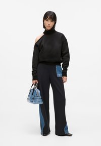 Fekete pulóver aszimmetrikus dizájnnal és gallérral, fekete nadrággal párosítva, amelyen farmer textúrájú zsebe van. Kék farmer táska.