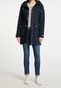 Granatowa wodoodporna parka z zamkiem z przodu, regulowanym kapturem, bocznymi kieszeniami i zapinana na napy. W połączeniu z obcisłymi dżinsami i białymi trampkami.