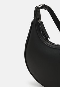 Sort halvmåneformet håndtaske med struktureret overflade, lynlås i toppen og justerbar rem med sølvspænde.