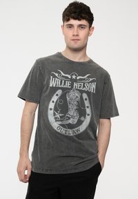 Gray cotton t-shirt featuring a cowboy boot graphic, "Willie Nelson" text, and "Outlaw" banner. Short sleeves and a crew neckline.