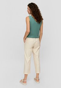 Un haut sans manches vert clair avec un col en V, associé à un pantalon crème longueur cheville. Des sandales confortables complètent la tenue.