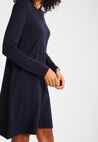 Abito lungo navy a maniche lunghe con scollatura tonda, silhouette a trapezio, texture morbida e design senza cuciture, che arriva a metà coscia. Nessun motivo o hardware visibile.