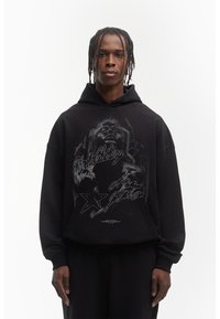 Felpa con cappuccio nera caratterizzata da una stampa grafica con stelle e testo. Vestibilità rilassata con polsini a costine e tessuto testurizzato.