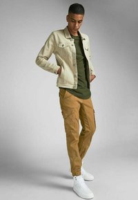 Light beige denim jacket, olive green t-shirt, and tan cargo pants. White sneakers. Casual fit with pockets on pants and button details on jacket.