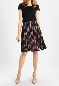 Svart topp i kombination med en knälång kjol med ett lager av gitterdesign i svart och rosa, dekorerad med ett smalt svart bälte.