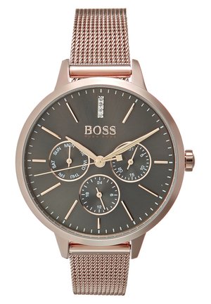Montre rose gold avec un cadran gris foncé, dotée de trois sous-cadrans, d'index en bâton et d'un bracelet en mailles. Accents en laiton et un détail en diamant unique.