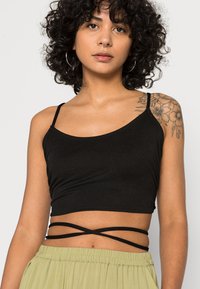 Top cropped preto com alças finas, apresentando um design ajustado e detalhes em camadas em cruz na cintura. Tecido suave.