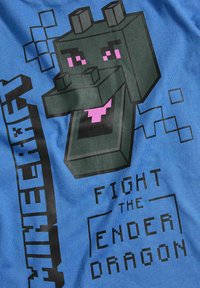 Camiseta de algodón azul con un diseño de dragón pixelado en verde con acentos en rosa y texto negro que dice "PELEA CONTRA EL ENDER DRAGON".