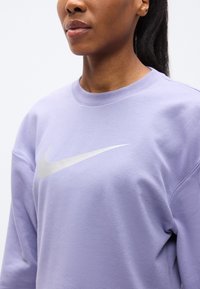 Μωβ μπλούζα Nike με υφασμάτινη υφή, στρογγυλή λαιμόκοψη και εμφανές ασημένιο λογότυπο στο στήθος.