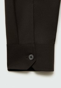 Poignet de chemise marron foncé avec un bouton noir. Présente un tissu net, un design structuré et une coupe angulaire au niveau du poignet.