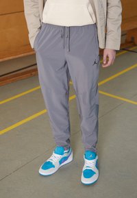 Grå joggebukser med elastisk talje og snor. Har et sort logo på venstre lår. Bruges sammen med blå og grå sneakers.