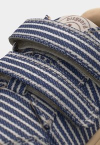 Gros plan sur des brides de sandales en tissu rayé bleu et blanc avec des fermetures ajustables et un marquage beige sur la semelle intérieure.