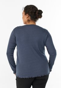 Marineblaues Langarmshirt mit Rundhalsausschnitt, das einen gewellten Saum und eine weiche Textur aufweist, designed für Komfort und lässiges Tragen.