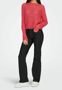 Roze, gestructureerde gebreide trui met open steken, cropped lengte en golvende zoom. Gecombineerd met een high-waisted zwarte spijkerbroek en witte sneakers.